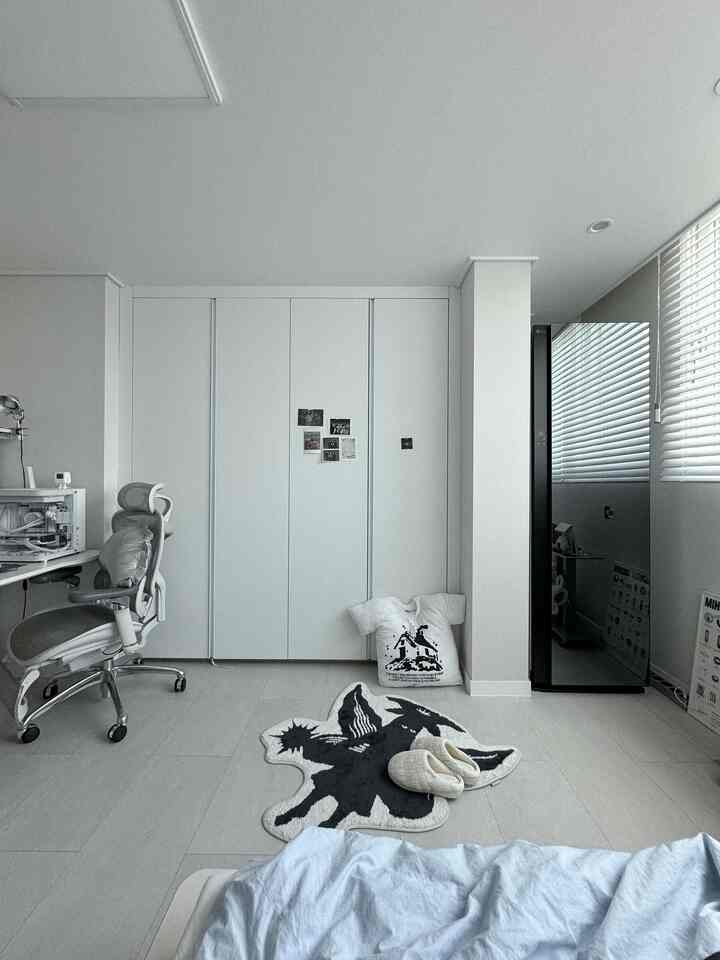 白い背景とモダンなビルトインクローゼットがある寝室、スタイラーとオフィスチェアが配置された清潔な空間