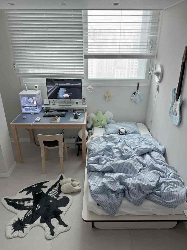 ホワイトとウッドトーンが調和した小さなワンルーム、ベッドとデスク、コンピュータが配置された落ち着いた在宅勤務空間