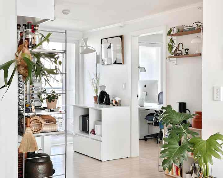 白とナチュラルトーンのキッチン兼ホームオフィススペース、美しい収納と植物が配置されたモダンな雰囲気のインテリア