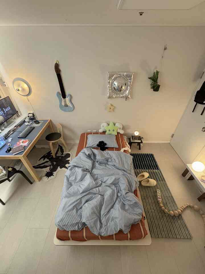 温かみのあるベージュ色調のナチュラルウッド家具がある一人用寝室、ベッドとデスク、壁のオブジェが配置された雰囲気のあるインテリア