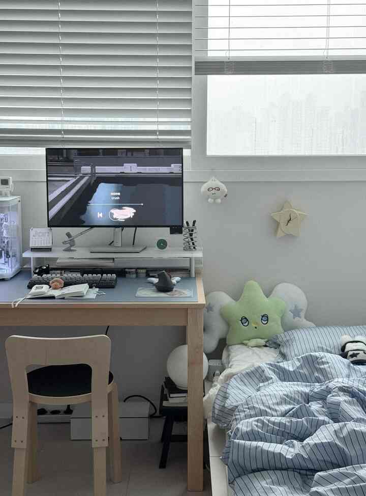 白いブラインドとナチュラルウッド調の机、ベッドが配置されたシンプルモダンな寝室のホームオフィス空間