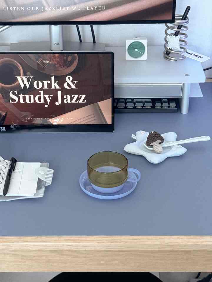 パステルブルーの色調のホームオフィス空間、モニタースタンドと机上のカップ、ノートが整理されたシンプルで落ち着いた作業空間