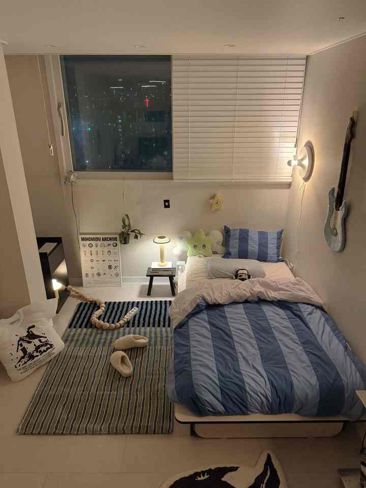 白を基調とした6畳の寝室、スカイブルーのストライプ柄寝具と子供向けの小物、暖かな照明が印象的な空間