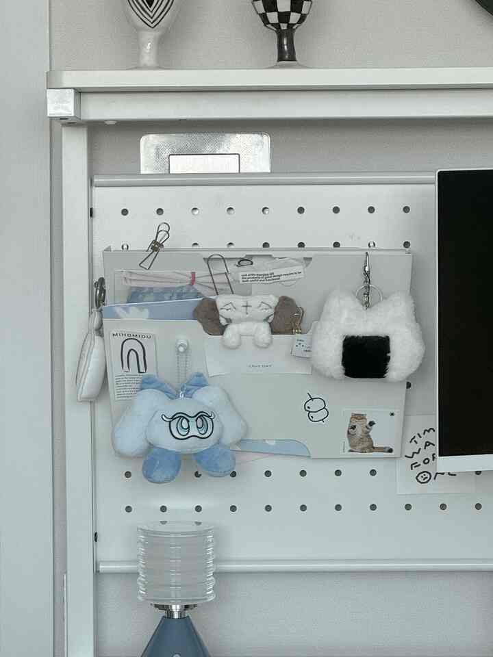 白いペグボードの壁にKVISSLE新聞ラックを掛け、手紙やぬいぐるみのキーチェーンを整理したシンプルなホームオフィス空間