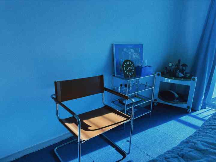 落ち着いたブルーのトーンのリビング、茶色のレザーアームチェアとメタルフレームのサイドテーブル、青いカーテンとカーペットが配置されたミッドセンチュリーモダンなインテリア