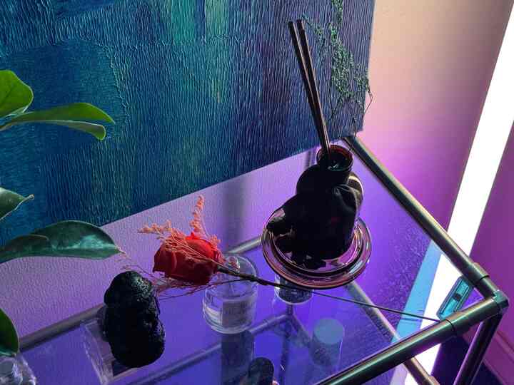 紫色の照明が照らすモジュール式ガラス棚にディフューザーと抽象画が配置されたモダンな空間