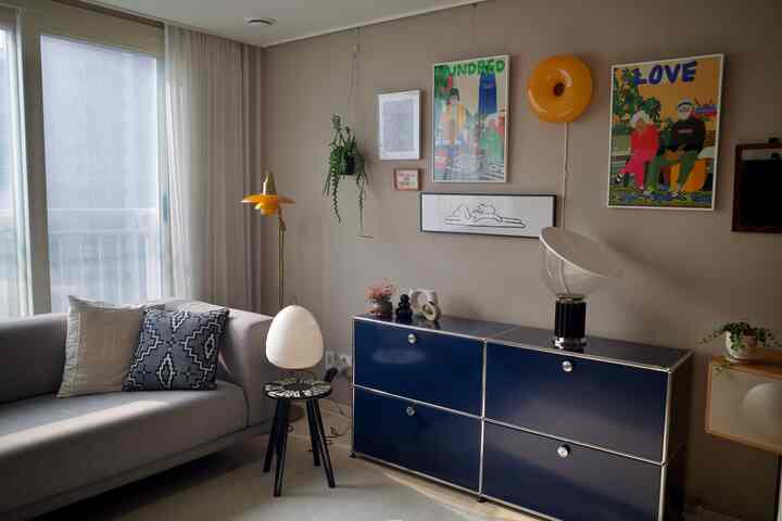 ネイビーブルーとベージュのトーンを持つリビング、グレーのソファとネイビーのサイドボード、アールデコ風のアートと照明が調和した印象的な空間