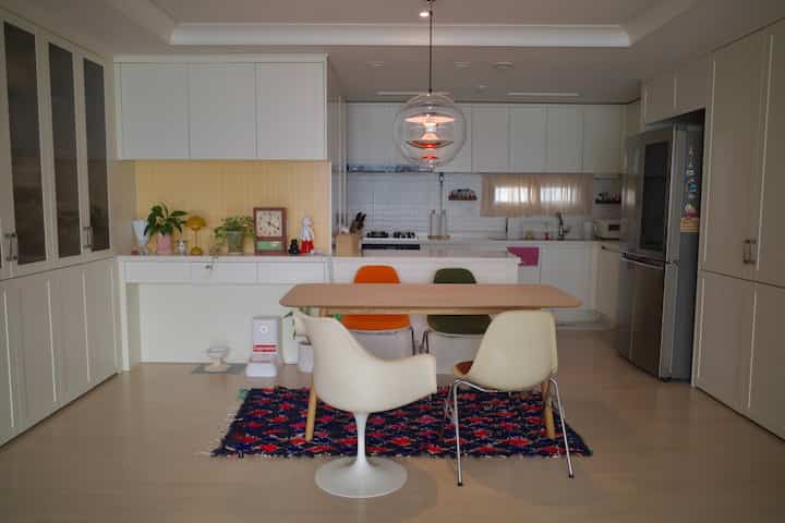 白と黄色のトーンのキッチンとダイニングルーム、多彩なダイニングチェアとヴィンテージ時計が配置されたモダンでナチュラルなインテリア