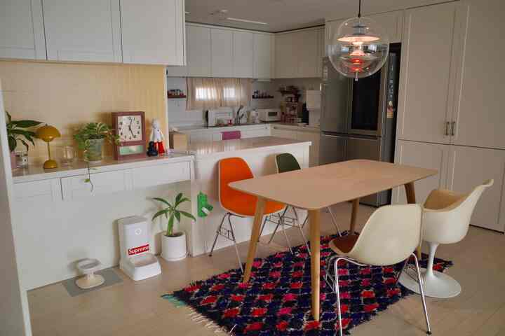 白とナチュラルトーンのダイニングルーム、オレンジとグリーンのダイニングチェアとカラフルなラグが調和した清潔感のある雰囲気のインテリア