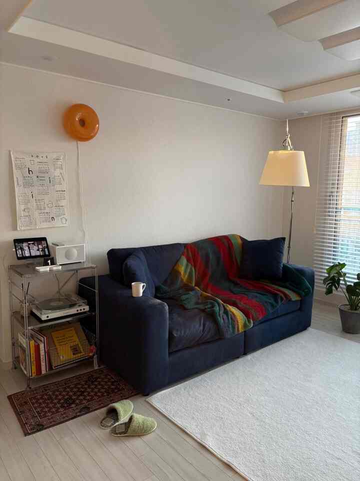 白い壁と床、ネイビーのソファとフロアランプが配置されたモダンで清潔感のあるリビング。