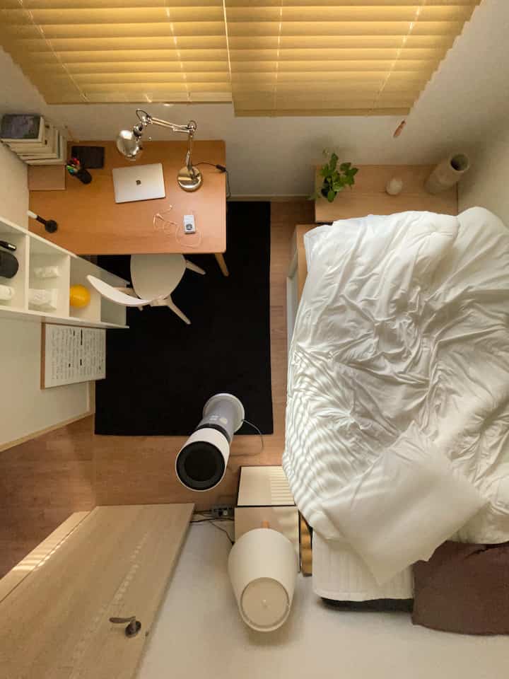 ホワイトのベッドと木目調のデスク、ブラインドが配置されたナチュラルでシンプルな6畳の寝室兼ホームオフィス