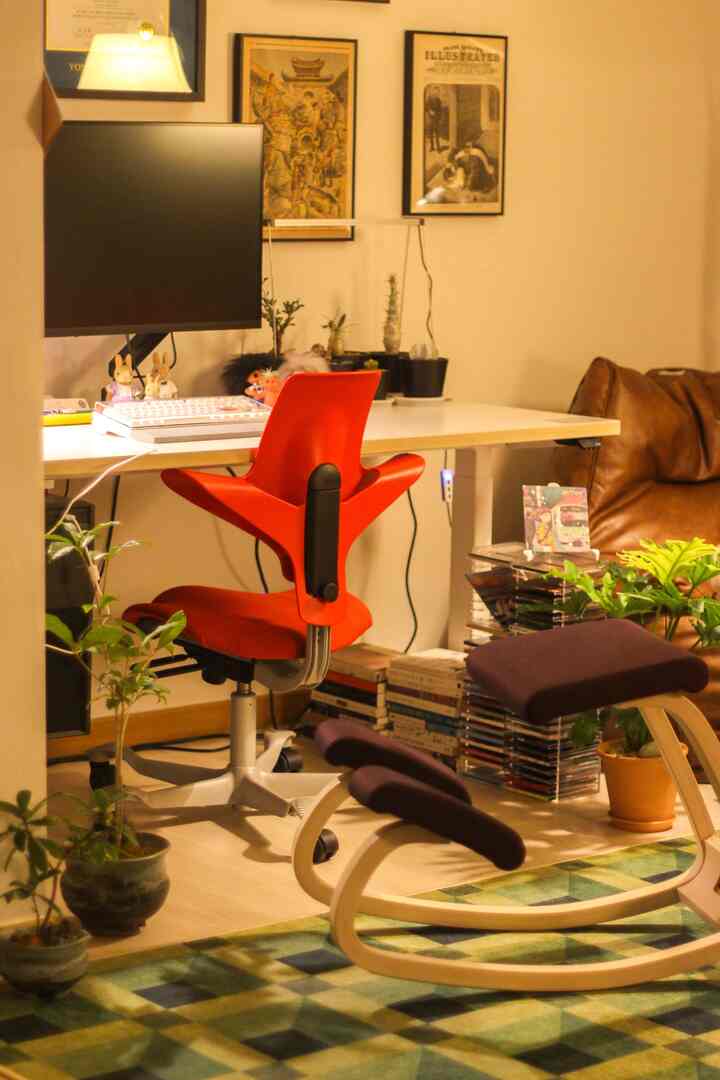暖かいブラウンとホワイトのトーンが広がる狭いホームオフィス、赤いチェアと昇降式デスクが配置された居心地の良い作業空間