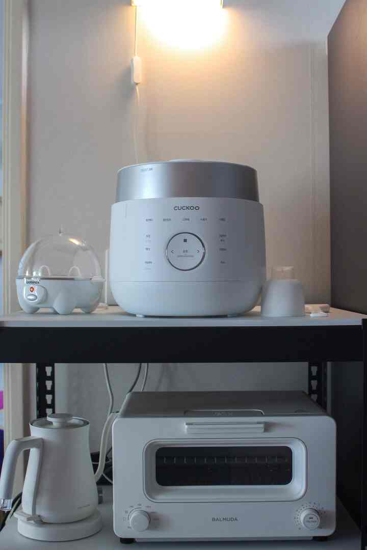 ホワイトとシルバーのトーンのキッチン、メタルシェルフに炊飯器とバルミューダのトースター、電気ケトルが整頓されている印象的なインテリア