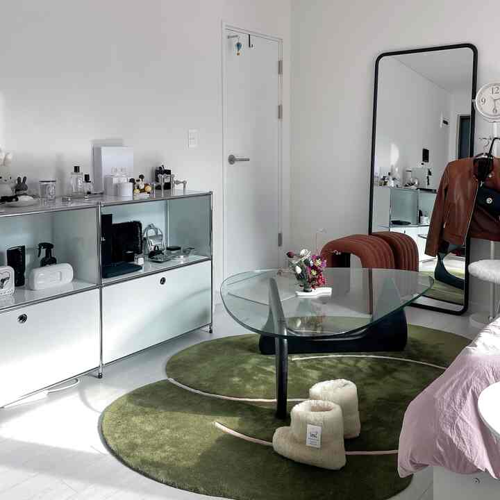 白と緑の落ち着いたリビング、ガラスのコーヒーテーブルと大きな全身鏡が配置されたシンプルな空間