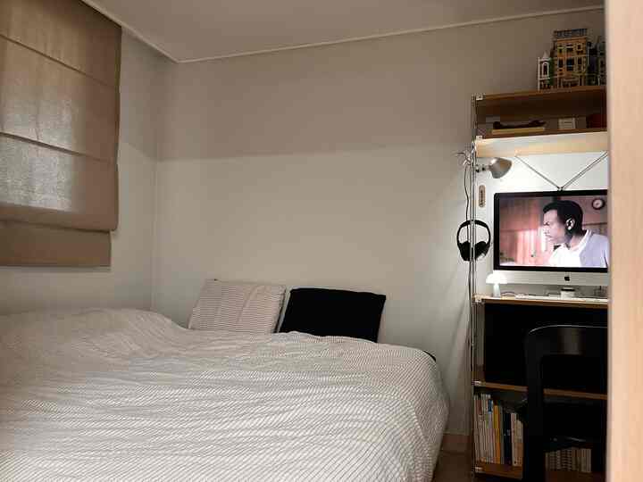 白とベージュの色調の寝室、左側にベージュのカーテン、右側にモダンなデスクとコンピューターが配置された落ち着いた空間