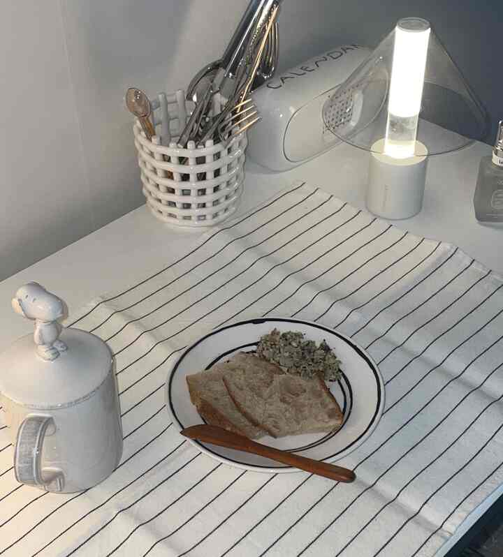 ホワイトトーンのキッチンスペース、白いテーブルの上にカトラリーとランプが配置された清潔で落ち着いた雰囲気のインテリア