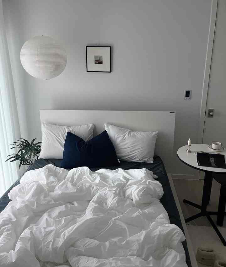 白とネイビーカラーのモダンで清潔感のある寝室、中央にベッドと小さなナイトテーブルが配置された空間