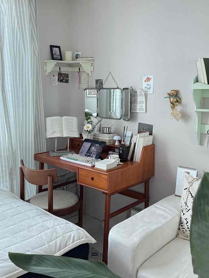 白と木目調の寝室内ホームオフィス、木製デスクと椅子、コーナーシェルフやヴィンテージラグが配置された雰囲気のあるインテリア