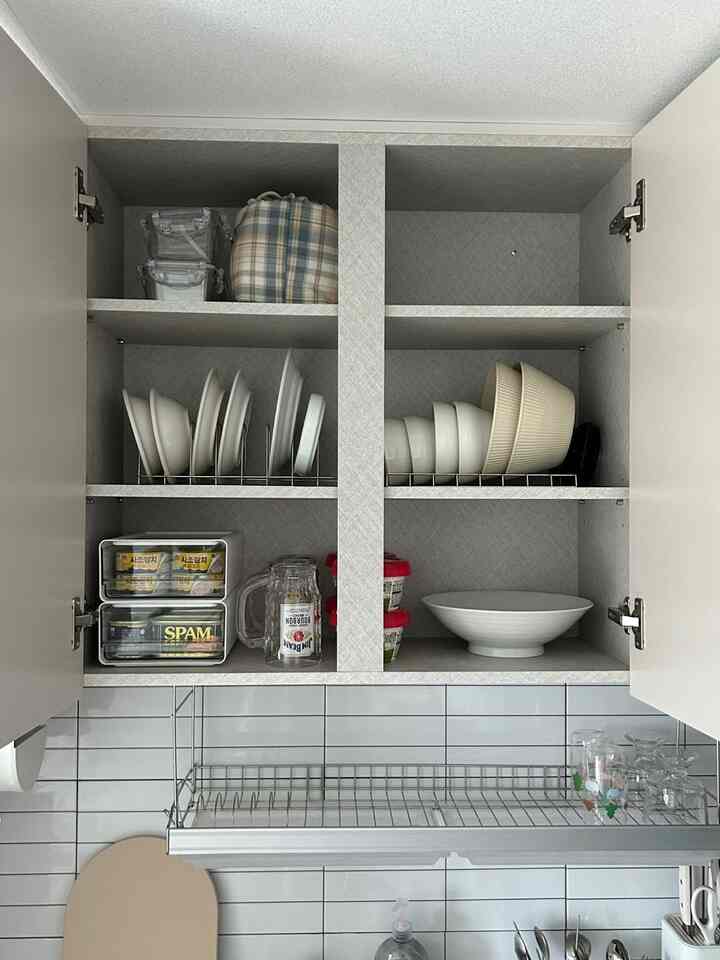 ホワイトとグレーのトーンのキッチン上部収納、皿とボウル、食品容器が整然と配置された空間