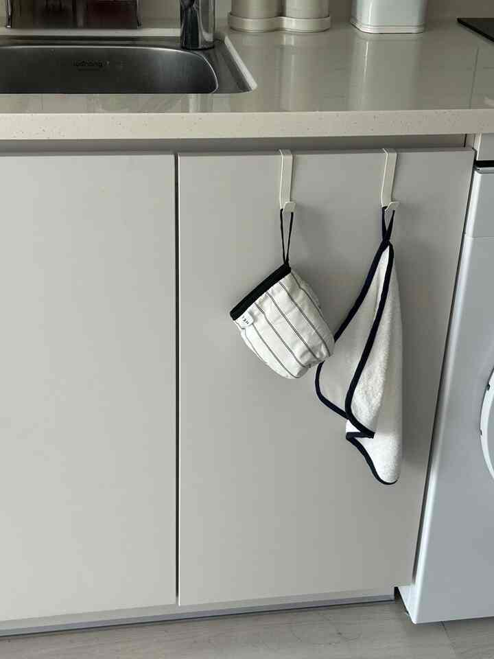 グレーとホワイトのトーンのキッチン、シンク下のキャビネットにキッチン手袋とハンドタオルが掛けられたシンプルで清潔感のある空間