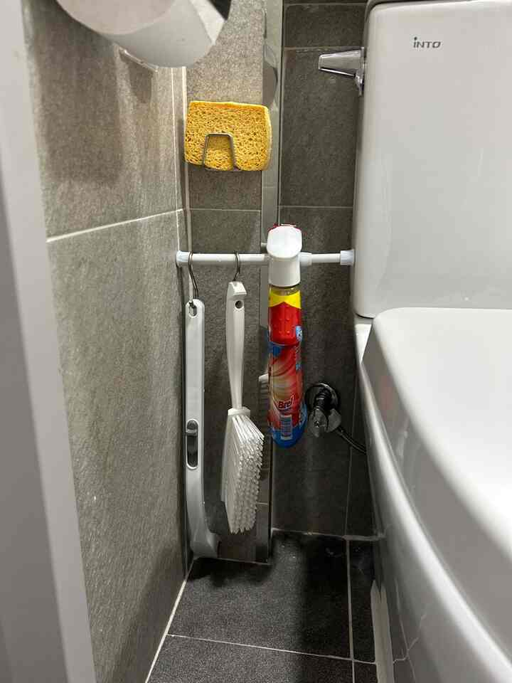 グレーのタイル壁と床のトイレの隅に圧縮棒で掃除用具とスポンジが整頓された清潔な空間