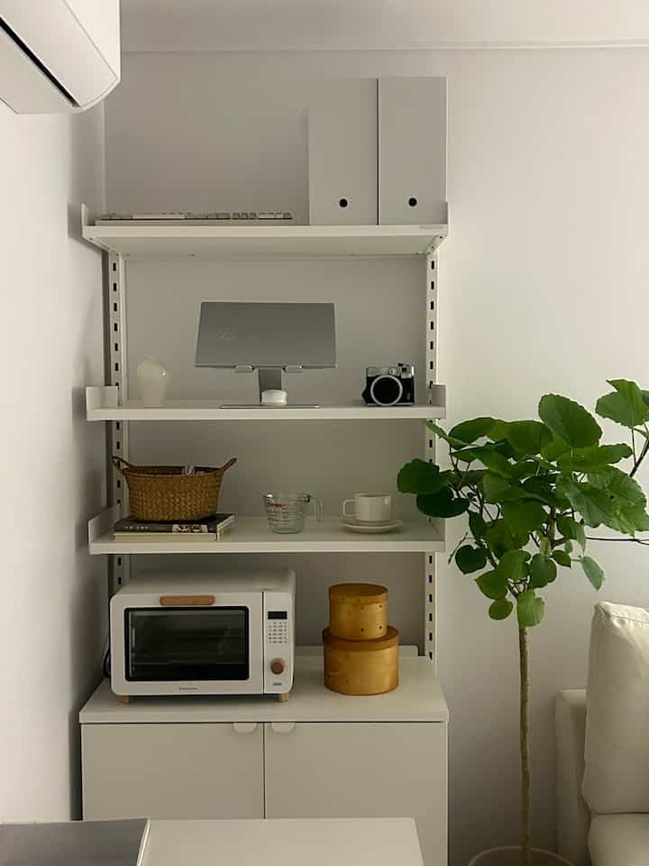 明るいホワイトとナチュラルカラーのキッチン収納棚と大きな緑の植物があるミニマルな空間