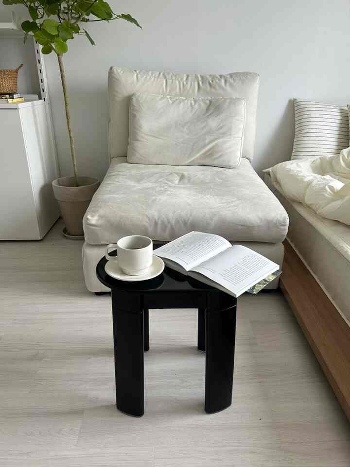 明るい白色調のリビングソファ空間、黒のコーヒーテーブルと自然素材の本棚が配置された落ち着いたインテリア