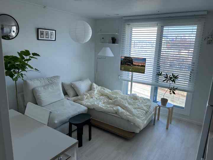 ホワイトとナチュラルウッドの調和が感じられるコンパクトな寝室、ベッドとソファ、フロアランプが配置された落ち着いたインテリア。