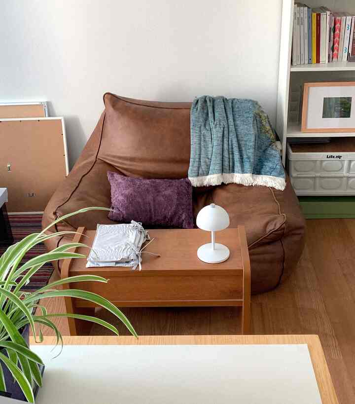 ブラウンのビーズクッションソファと木目調のサイドテーブル、白い壁が配置された明るい印象のコンパクトな寝室
