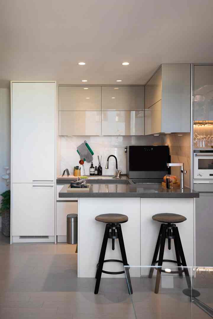 白とグレーのトーンのモダンなキッチン、食器洗い機と2つのスツールが配置された清潔感のある空間