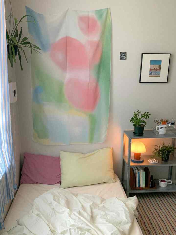 明るく爽やかな色調の寝室、白い寝具とピンク・イエローの枕、壁に夏の雰囲気のファブリックポスターが掛けられた温かみのあるインテリア