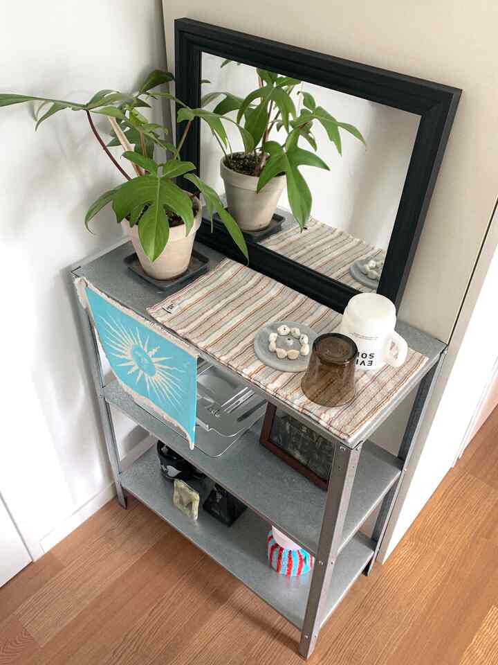 グレーの金属棚と黒い額縁の鏡、植物が置かれた玄関のウェルカムゾーンのインテリア