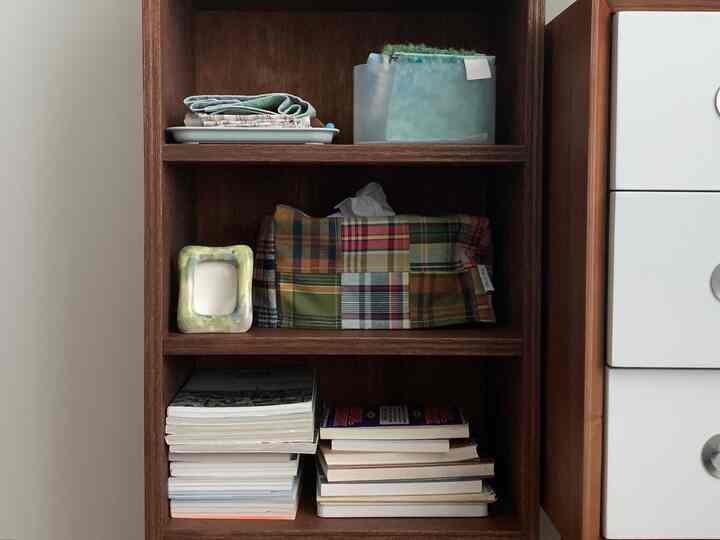 ブラウンの木目調本棚が配置された収納アイデアのある空間、パッチワークのティッシュケースと積み重ねられた本が印象的