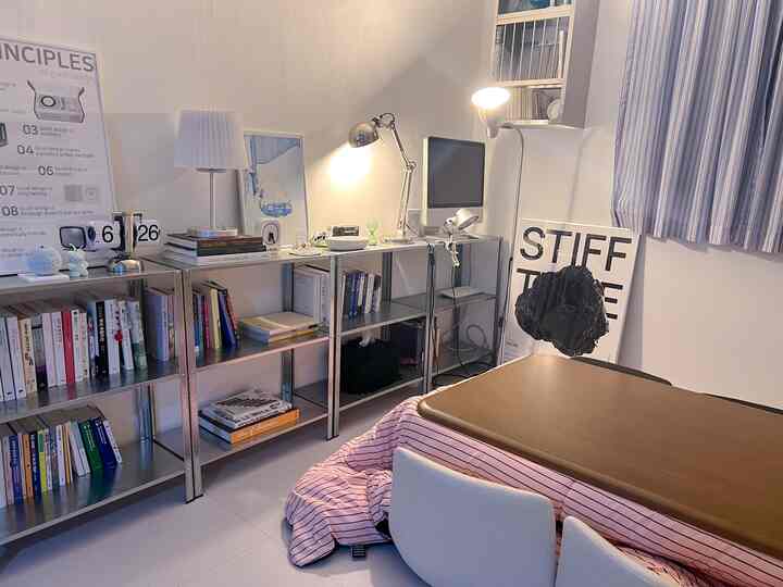 白とメタルのトーンが調和した狭いホームオフィスの空間で、長方形のこたつテーブルと本棚が配置された清潔感のあるインテリア。