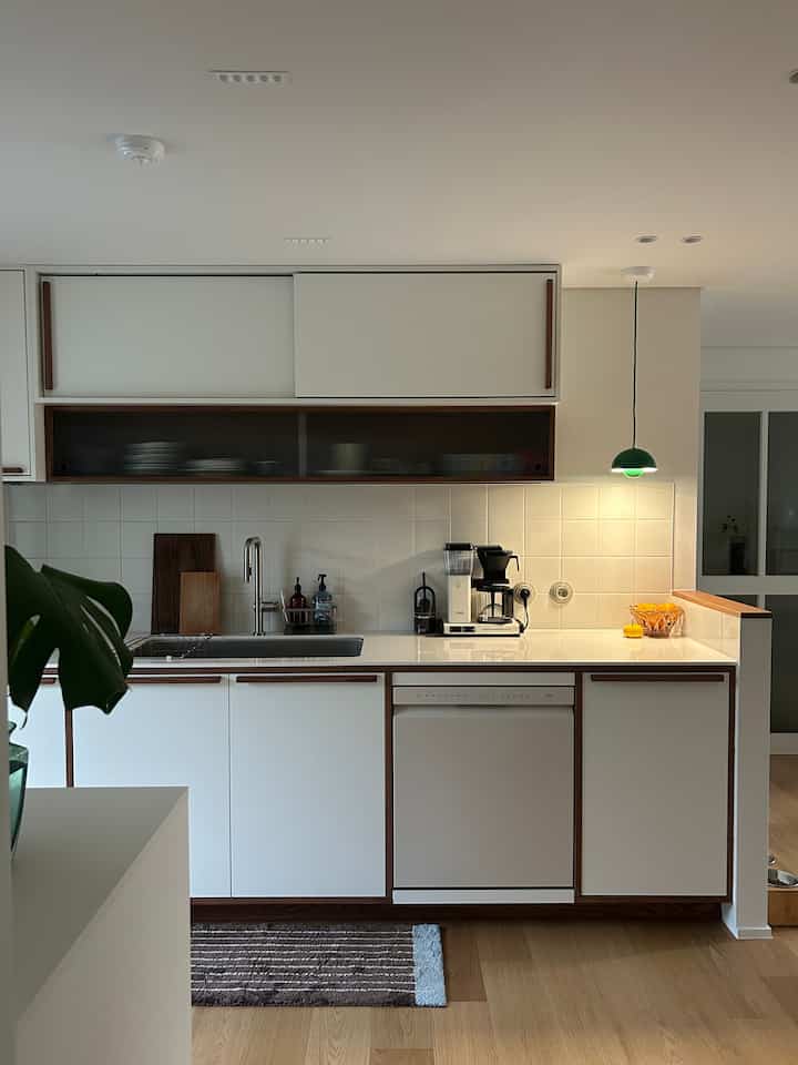 ホワイトと木目調が調和したキッチン、ペンダントライトとコーヒーマシンが配置されたモダンな空間