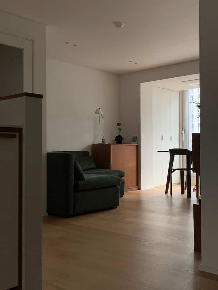 ナチュラルな木目調の床とダークグリーンのソファが配置されたモダンな1LDKのリビング