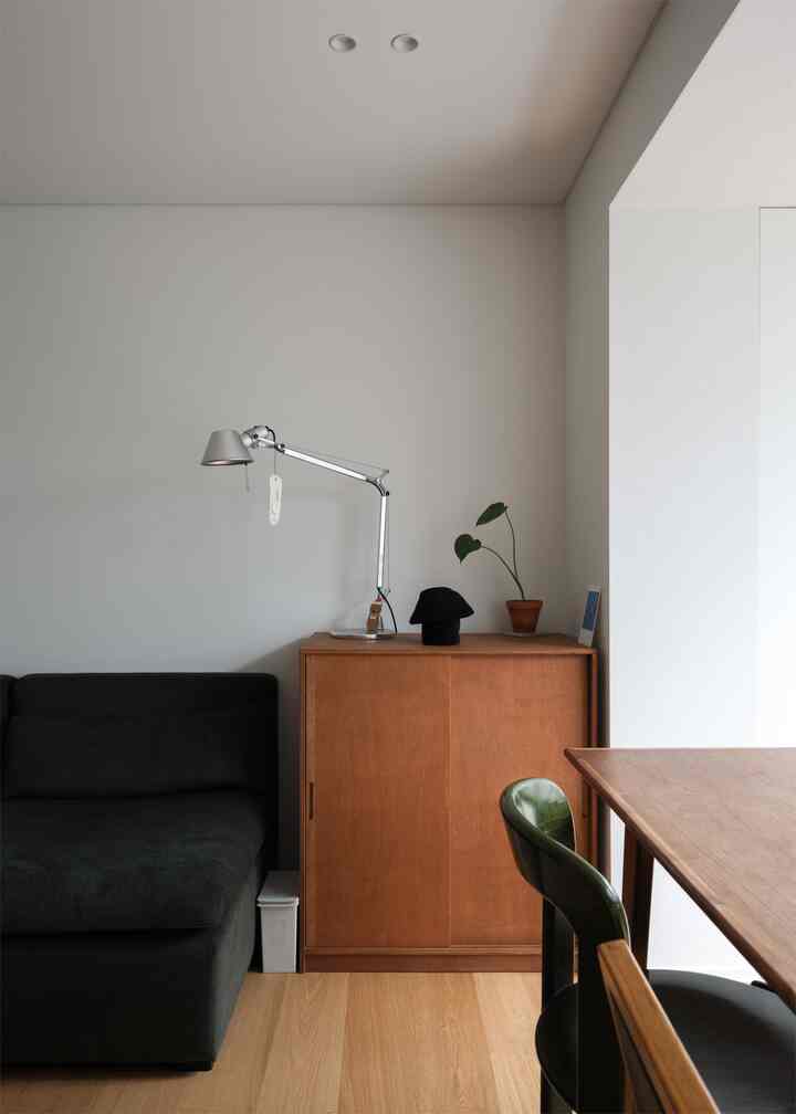 白い壁と温かみのあるブラウンの木目調が調和するリビング、濃い色のソファとラワン合板のサイドボードが配置された雰囲気のあるインテリア