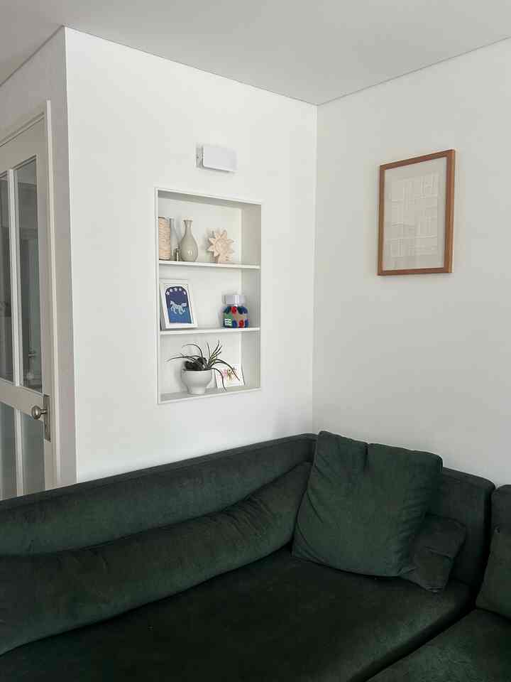 白い壁とダークグリーンのソファが配されたリビング、壁面の棚と額縁が自然な雰囲気を醸し出す印象的な空間