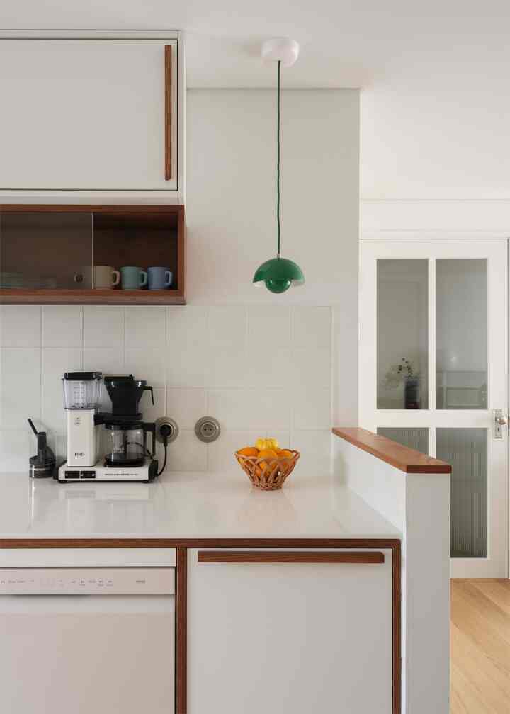 白と木目調が調和したキッチン空間、木製の取っ手とグリーンのペンダントライトがアクセントの清潔感あるインテリア