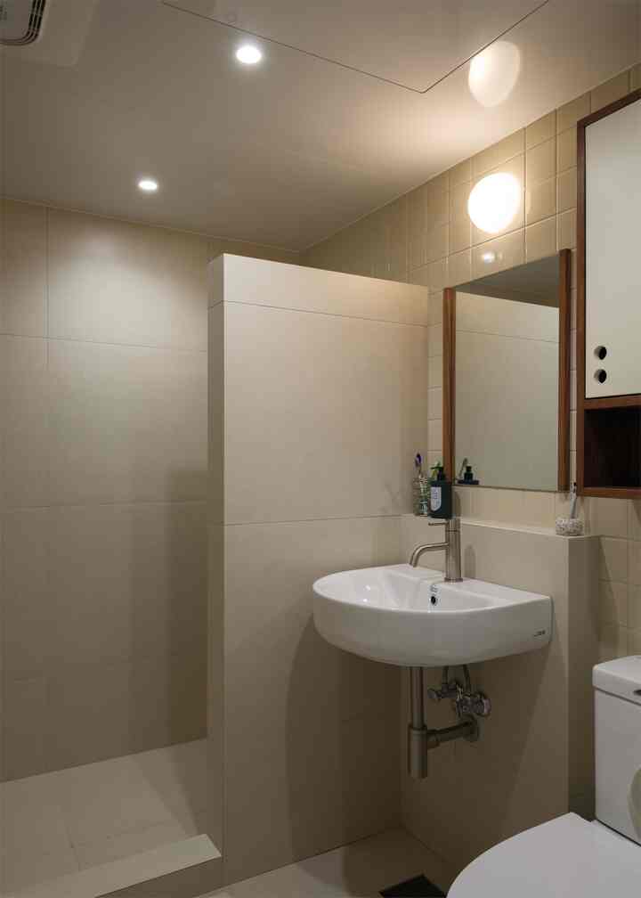 ベージュと白を基調としたトイレの内装、洗面台、モザイクタイル、木製の鏡と収納が配置された自然な雰囲気のインテリア