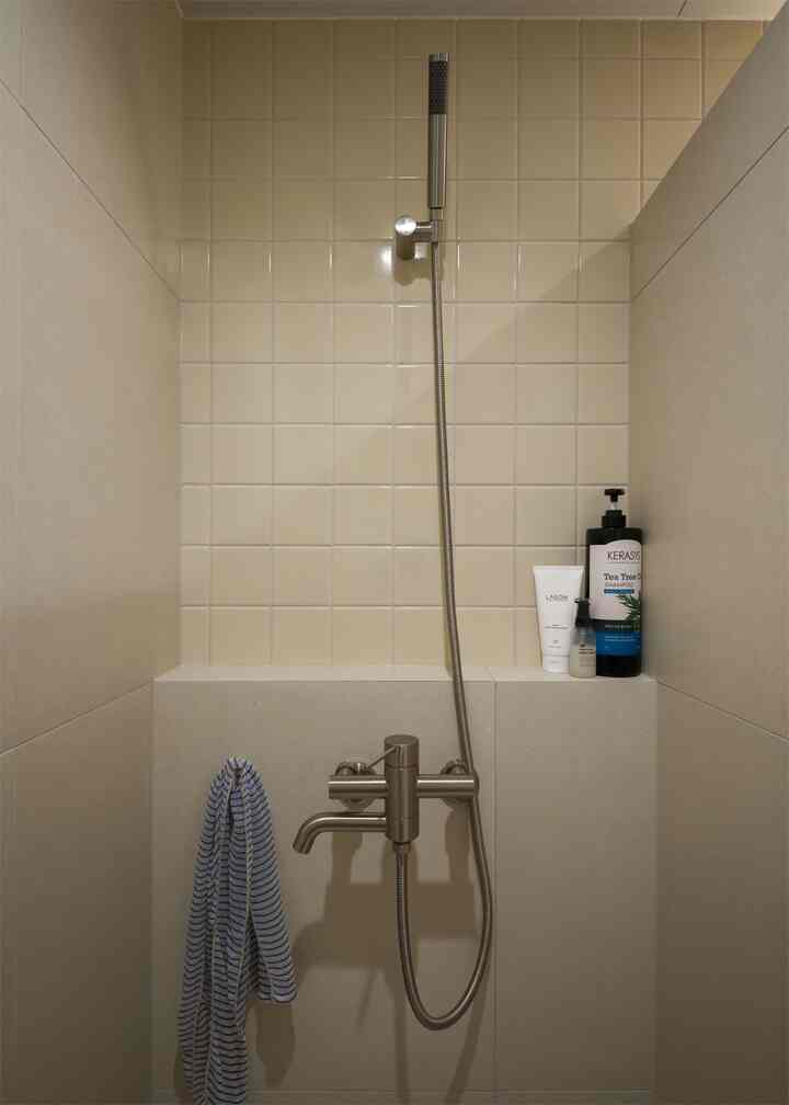 ベージュとクリーム色のタイルで構成されたモダンな浴室のシャワースペース、中央にシャワー水栓とハンドシャワーが配置された雰囲気のあるインテリア。