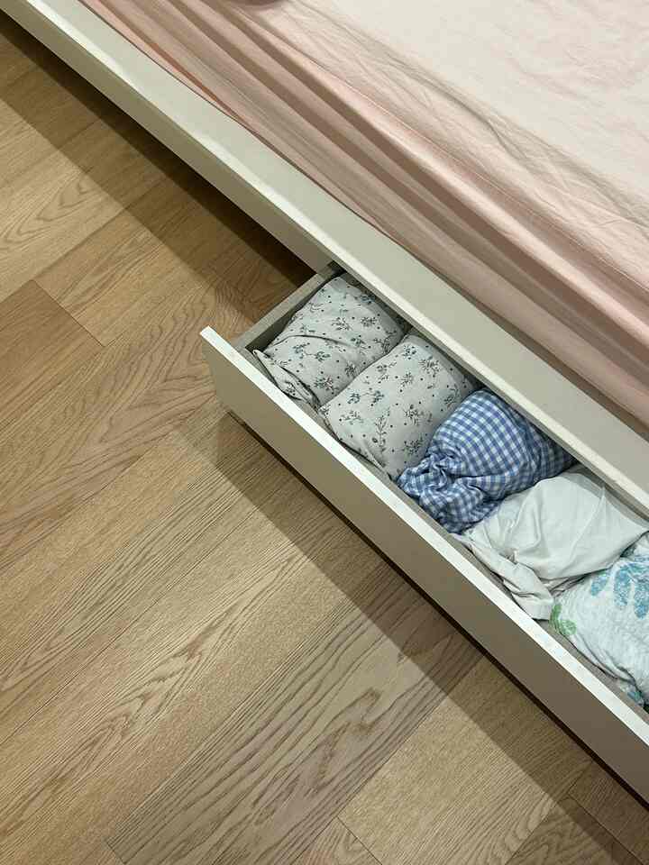 ナチュラルカラーの床とベッド下収納引き出しがあるピンクの寝具の印象的な寝室