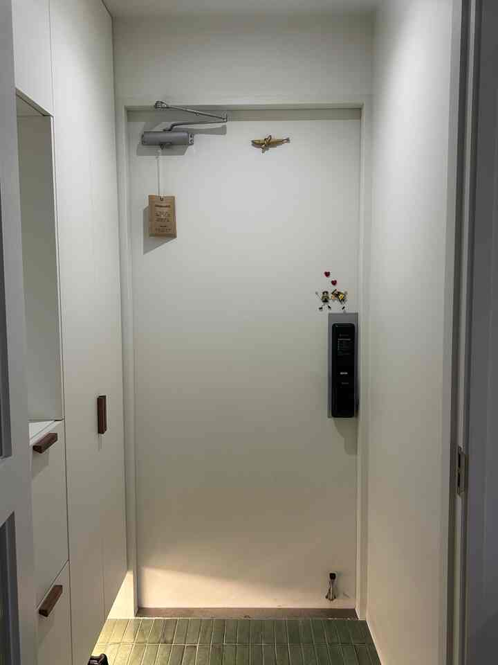 白とナチュラルカラーのタイルが調和するモダンな玄関、左壁に実用的なシューズラックが配置されている