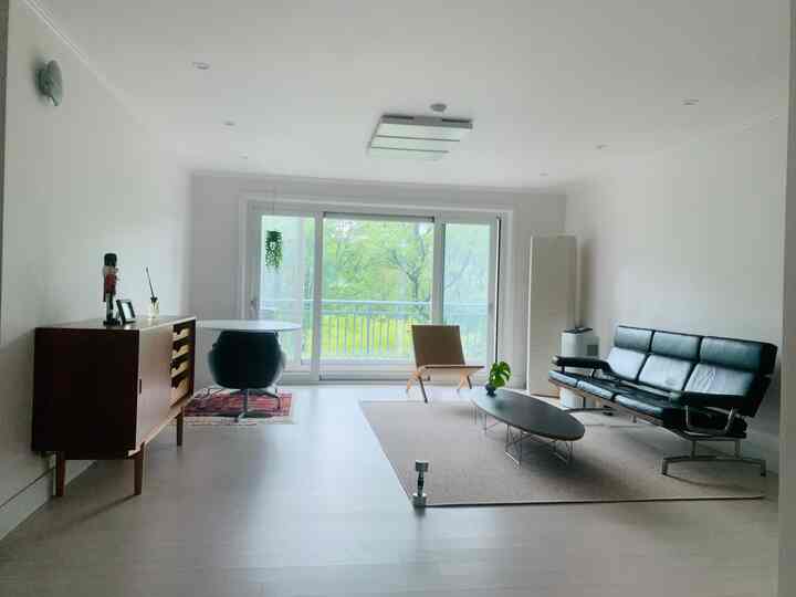 明るいナチュラルカラーとブラック家具が調和するモダンなリビング、広いガラス窓から自然光が差し込む空間