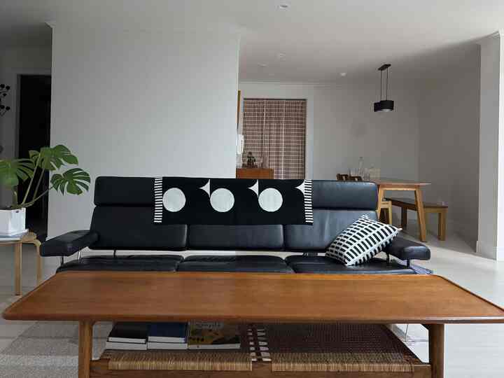 ブラックレザーソファと木製コーヒーテーブルが配置されたリビング、グラフィックパターンスローとクッションがアクセントのナチュラルでミッドセンチュリーモダンな空間