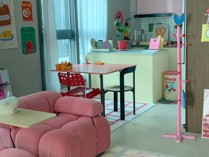 明るいピンクのソファとカーテンが配置された、2人暮らし向けのアットホームなワンルームキッチン・ダイニング