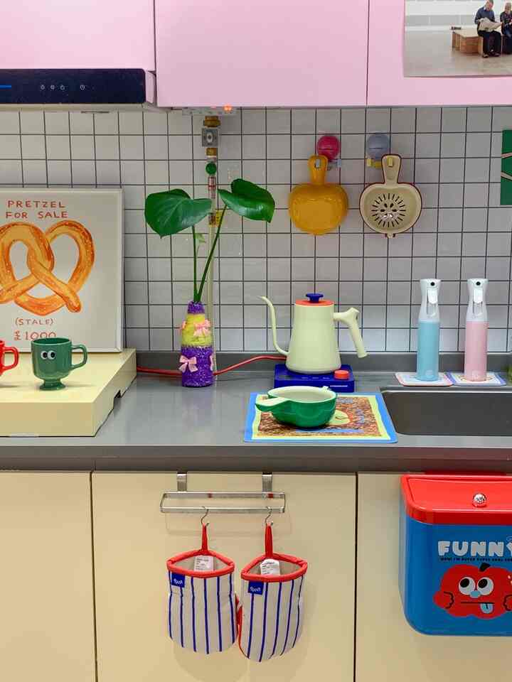 ピンク色の上部キャビネットと黄色のキッチン小物が調和するかわいらしいキッチン空間