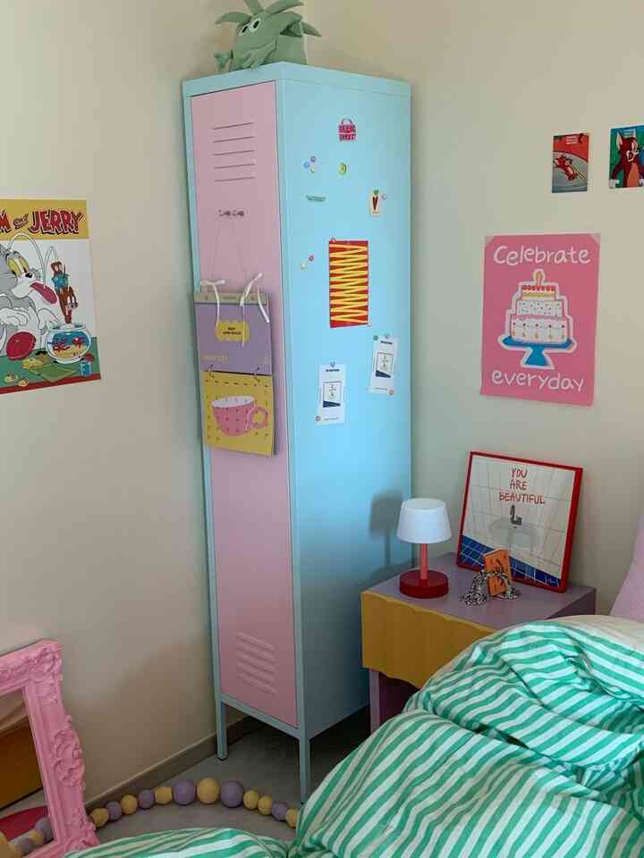 パステル調のピンクとアイボリー色の壁がある書斎、カラフルな鉄製収納棚とベッド、テーブルランプが配置された雰囲気のあるインテリア