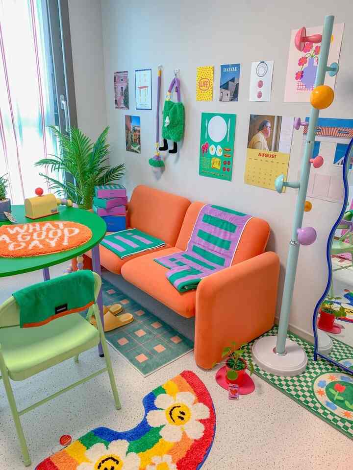 オレンジ色のソファと多彩なラグ、ポスターが配置されたカラフルなリビングルーム