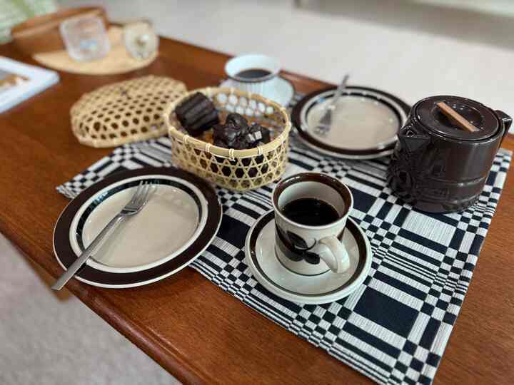 ブラウンの木目調テーブルにヴィンテージスタイルのコーヒーカップと皿、ラタンかごが置かれた雰囲気のあるおうちカフェ